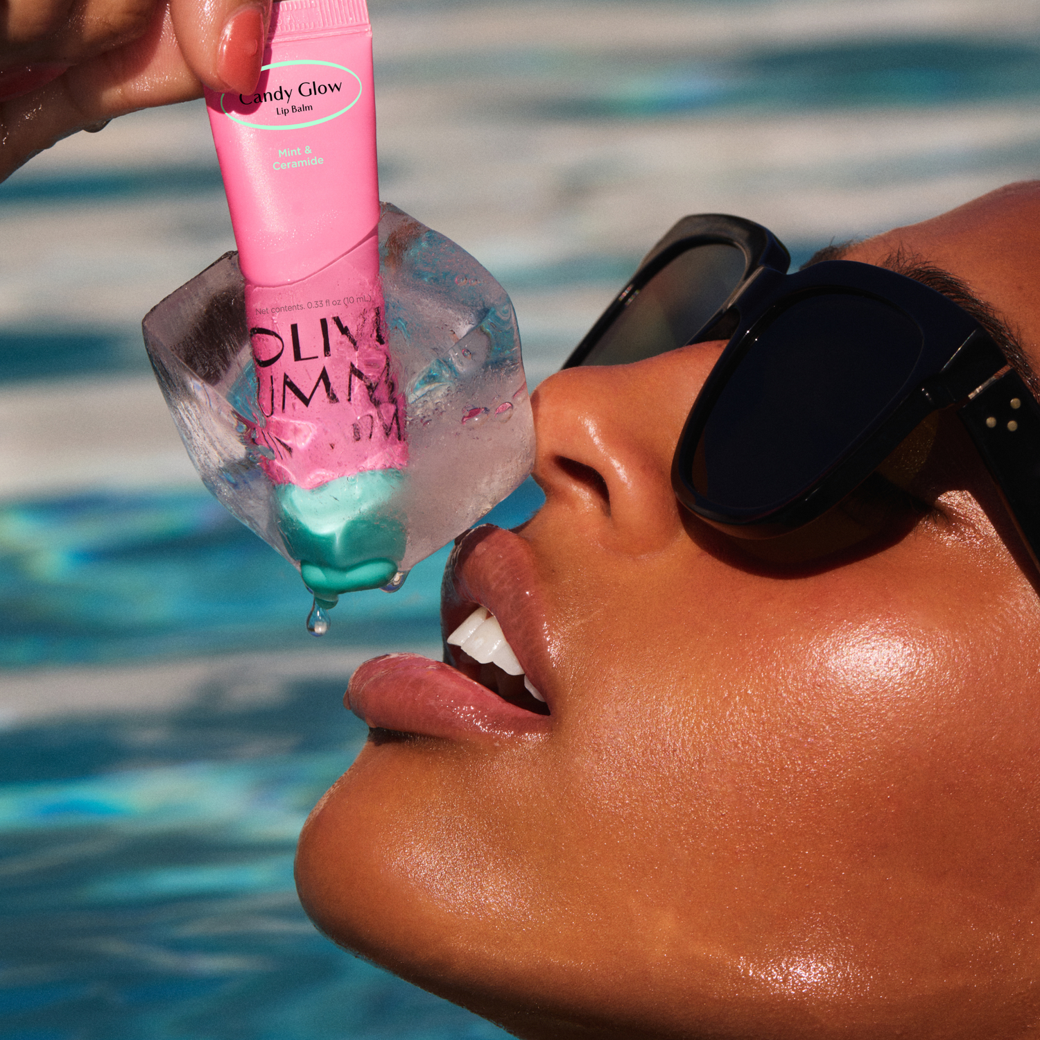 Person applying a pink lip balm labeled 'Fruity Glow' by Olivia umma to their lips with a pool in the background.