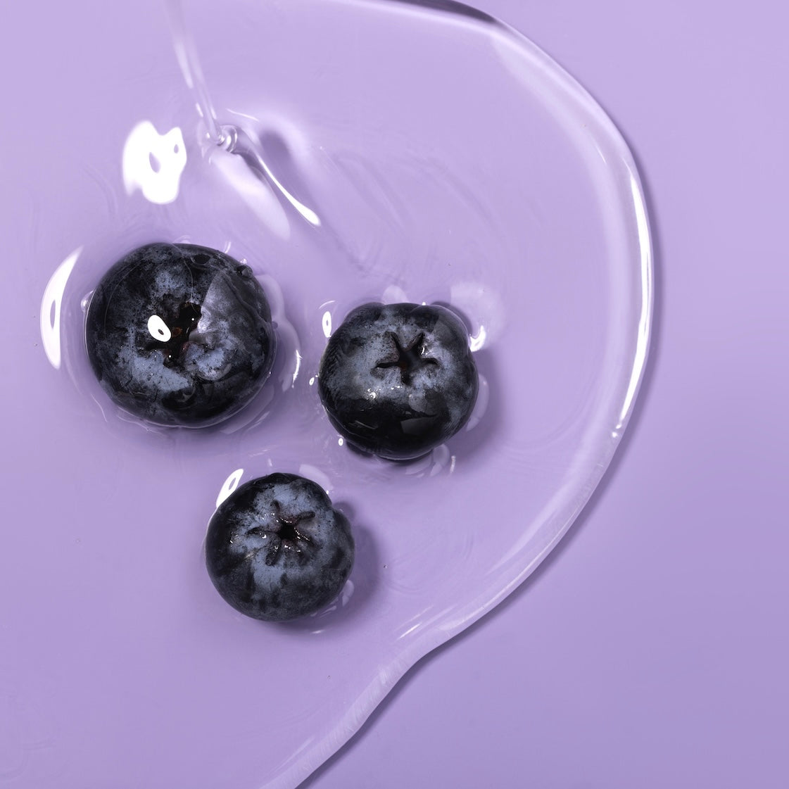 Three blueberries on a purple surface with a clear liquid.