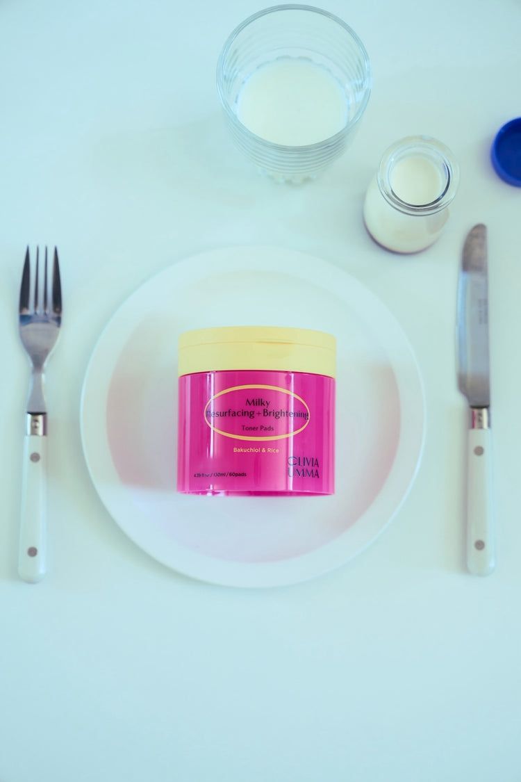 Milky Resurfacing + Brightening Toner Pads on a white plate with utensils and a glass of milk on a white background
