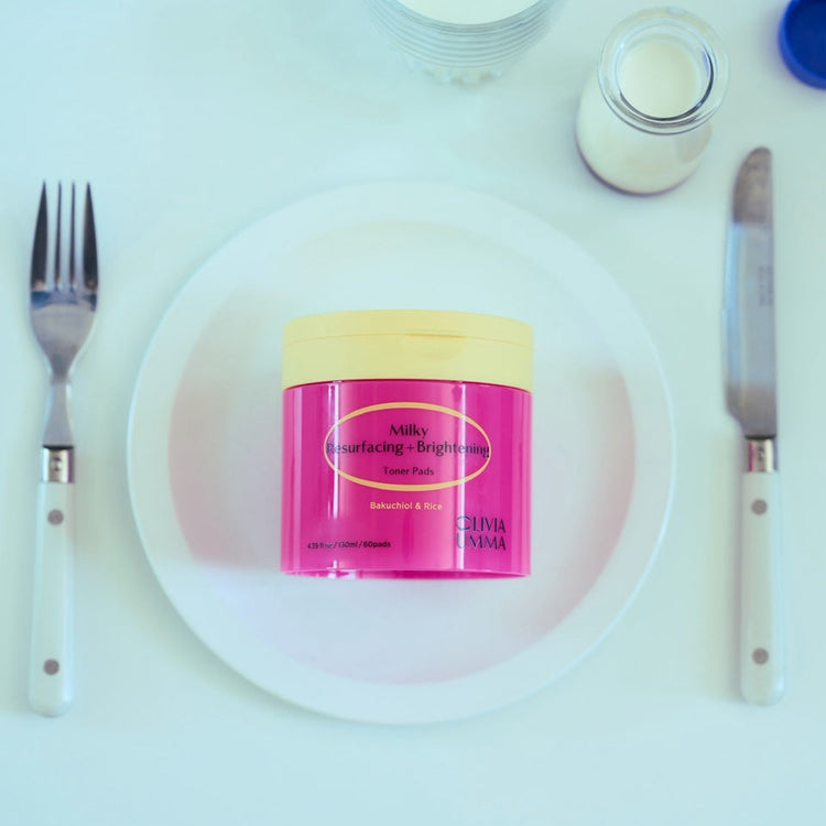 Milky Resurfacing + Brightening Toner Pads on a white plate with utensils and a glass of milk on a white background