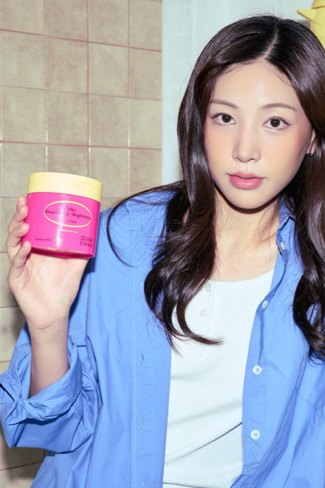 Woman holding a Milky Resurfacing + Brightening Toner Pads, wearing a blue shirt.