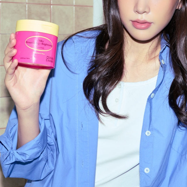 Woman holding a Milky Resurfacing + Brightening Toner Pads, wearing a blue shirt.