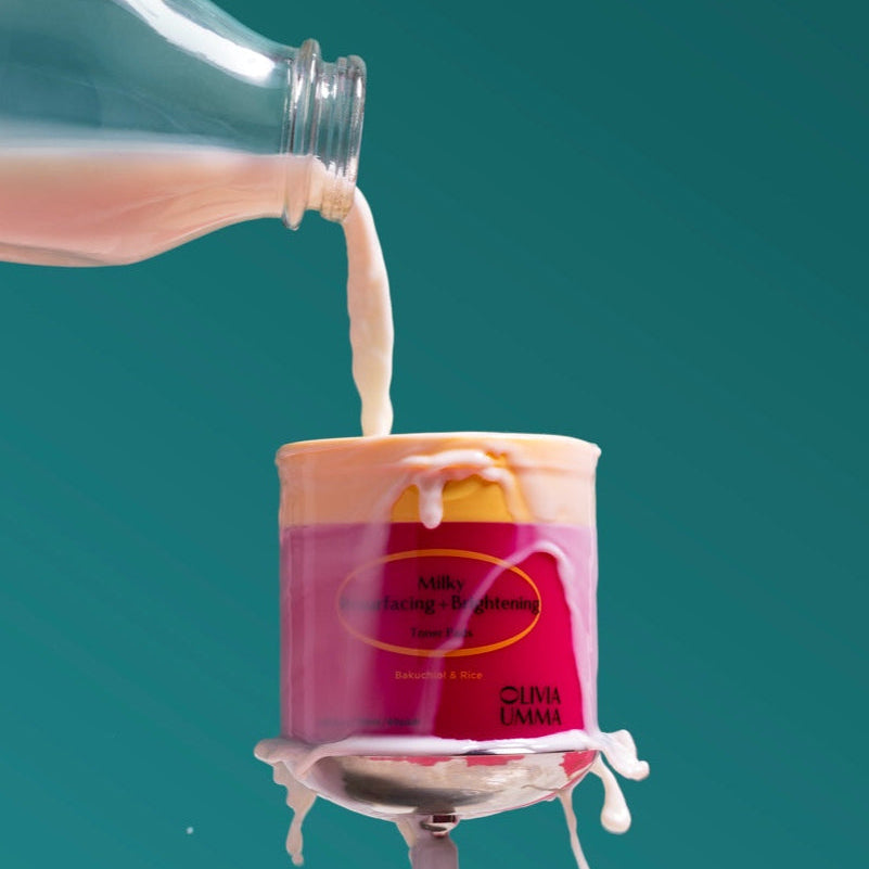 Bottle pouring milk into a pink container with a blue background, Milky Resurfacing + Brightening Toner Pads