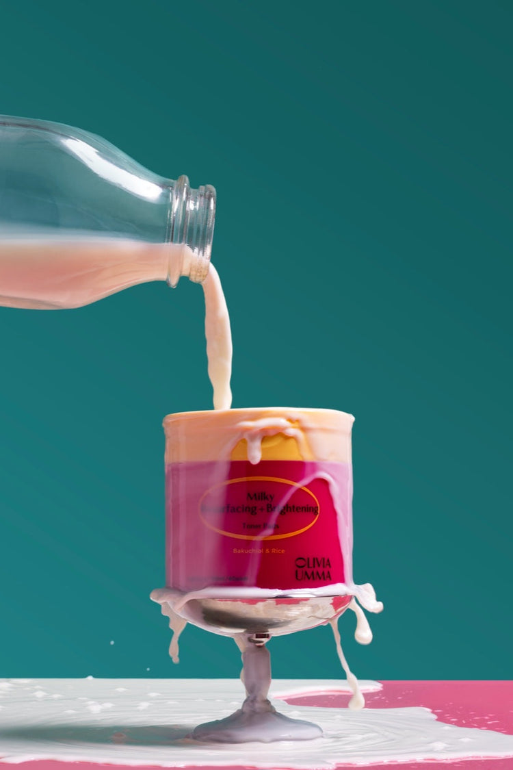 Bottle pouring milk into a pink container with a blue background, Milky Resurfacing + Brightening Toner Pads