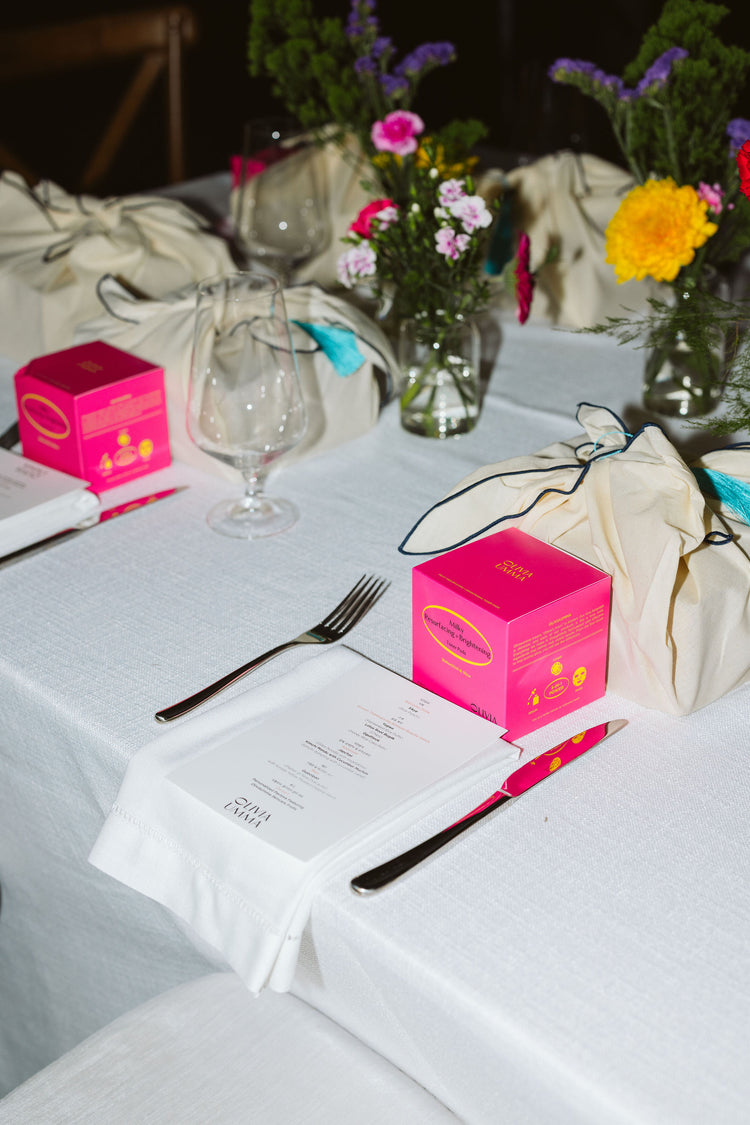 Table setting with Milky Resurfacing + Brightening Toner Pads, silverware, and floral arrangements on a white tablecloth.