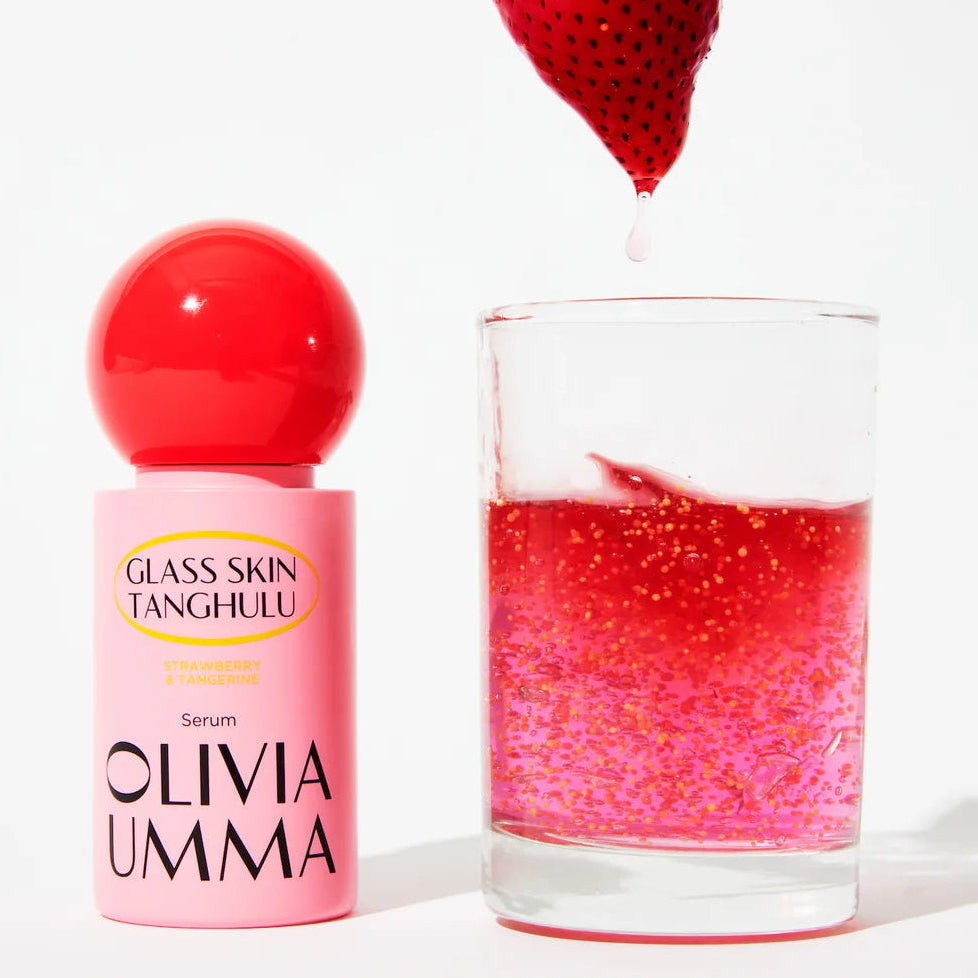 Olivia Umma serum bottle with a glass of pink liquid and a strawberry on a white background