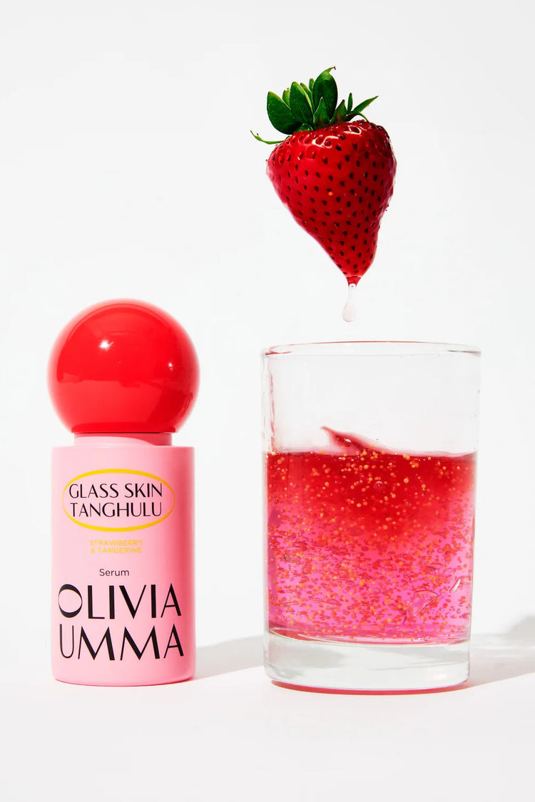 Olivia Umma serum bottle with a glass of pink liquid and a strawberry on a white background