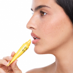 Woman applying a yellow lip product to her lips with a white background