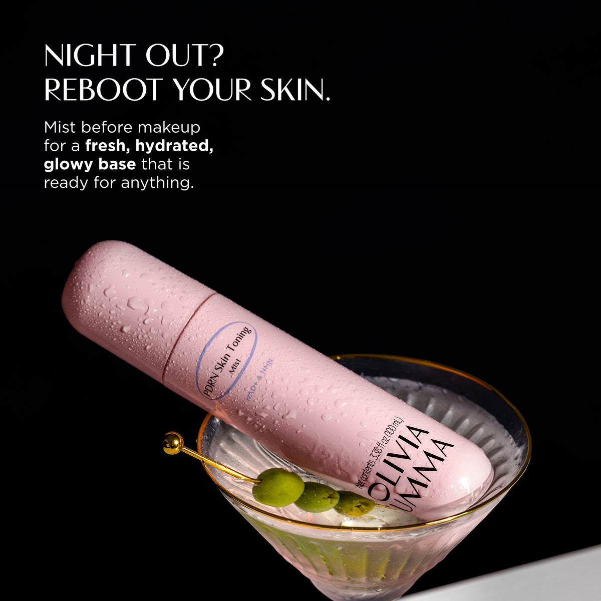 Olivaomma 99% Humidifying Mist in a light pink cylindrical bottle with water droplets, presented diagonally in a martini glass with olives on a black background with NIGHT OUT? REBOOT YOUR SKIN
