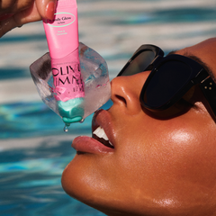 Person applying a pink lip balm labeled 'Fruity Glow' by Olivia umma to their lips with a pool in the background.