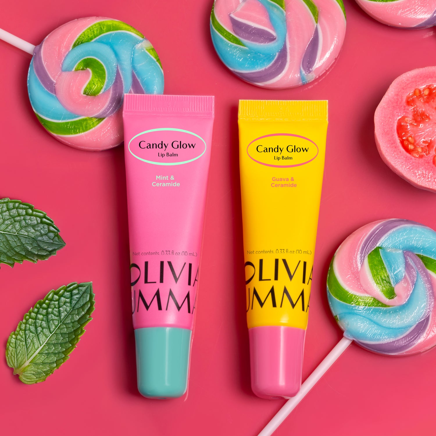 Two lip balms from Candy Glow on a pink background with colorful lollipops and mint leaves.