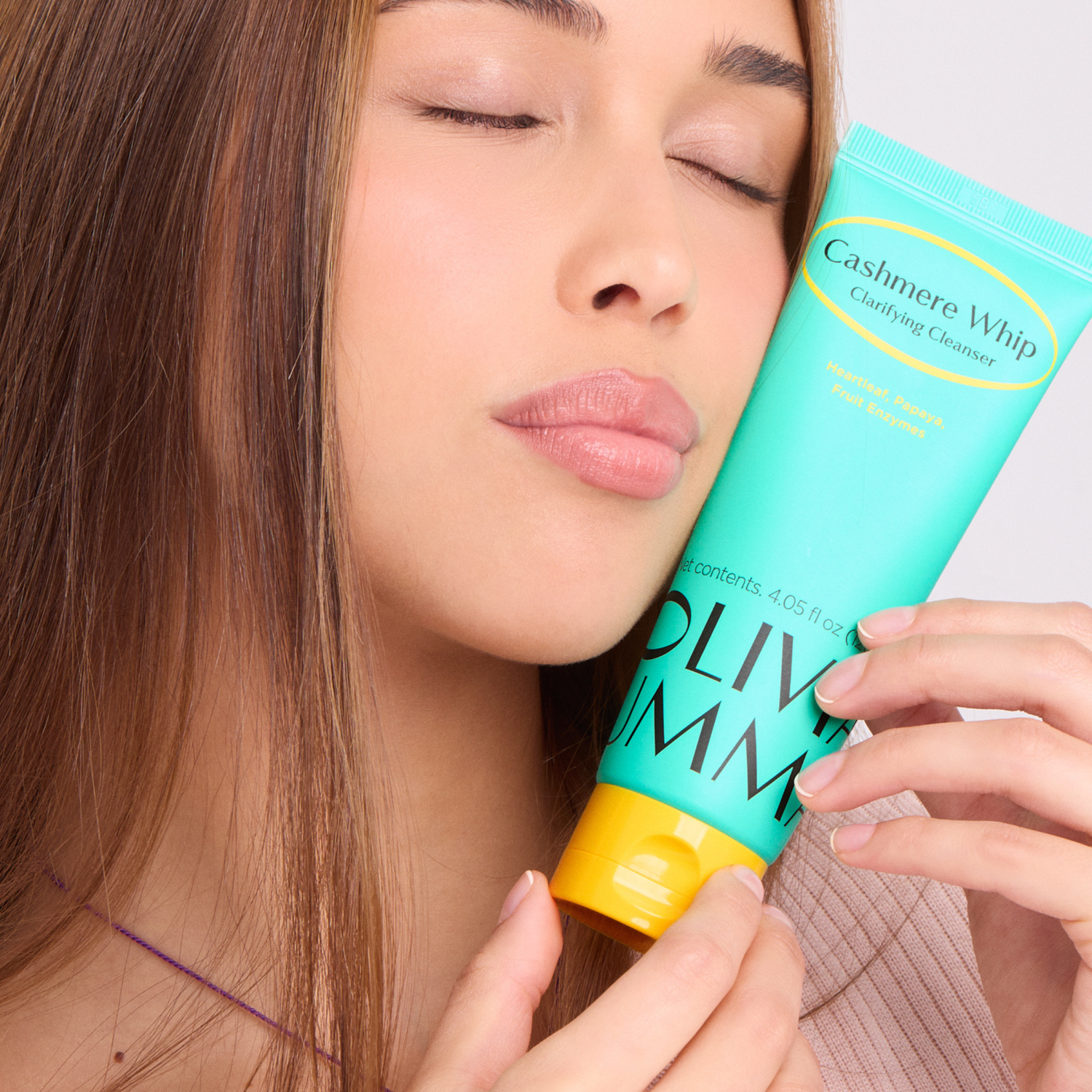 Woman holding a tube of Oliviamm cashmere whip clarifying cleanser product close to her face.