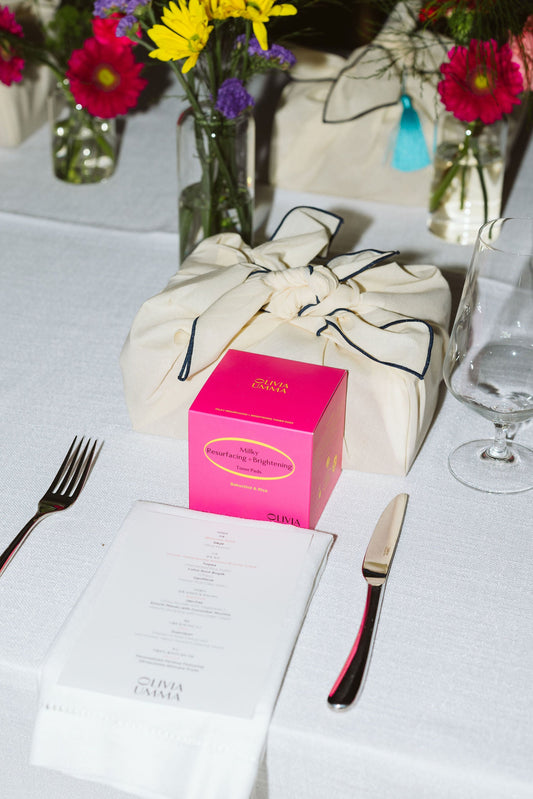 Table setting with flowers,Milky Resurfacing + Brightening Toner Pads, and cutlery on a white tablecloth.